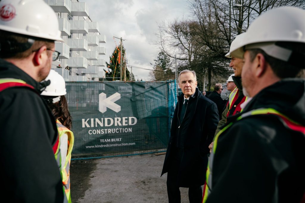 Prime Minister of Canada standing in front of fence signage at residential building