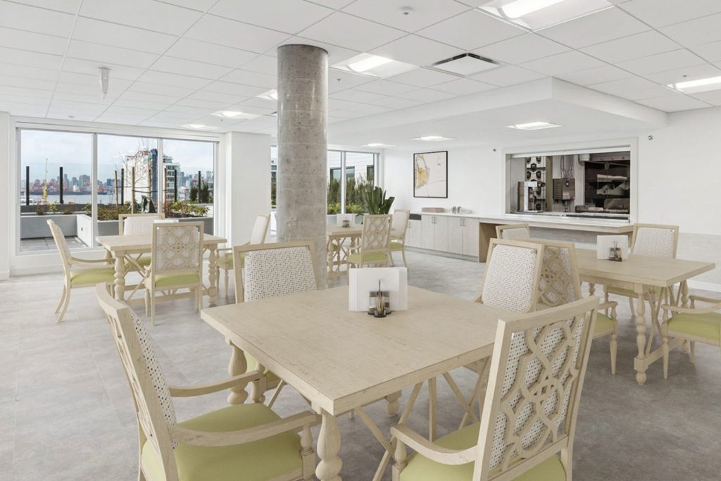 Communal dining room with natural wood tables and chairs, floor-to-ceiling windows overlooking Burrard Inlet