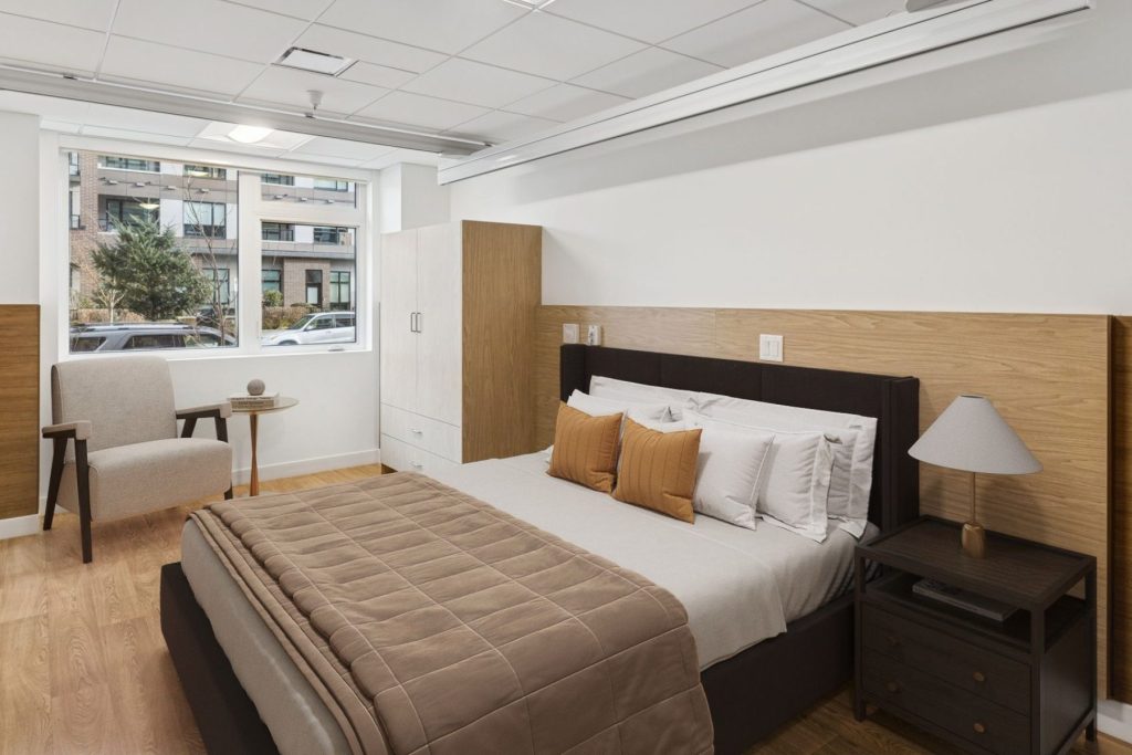 Modern bedroom with warm wood accents, neutral bedding, hardwood floors and a bright street-facing window